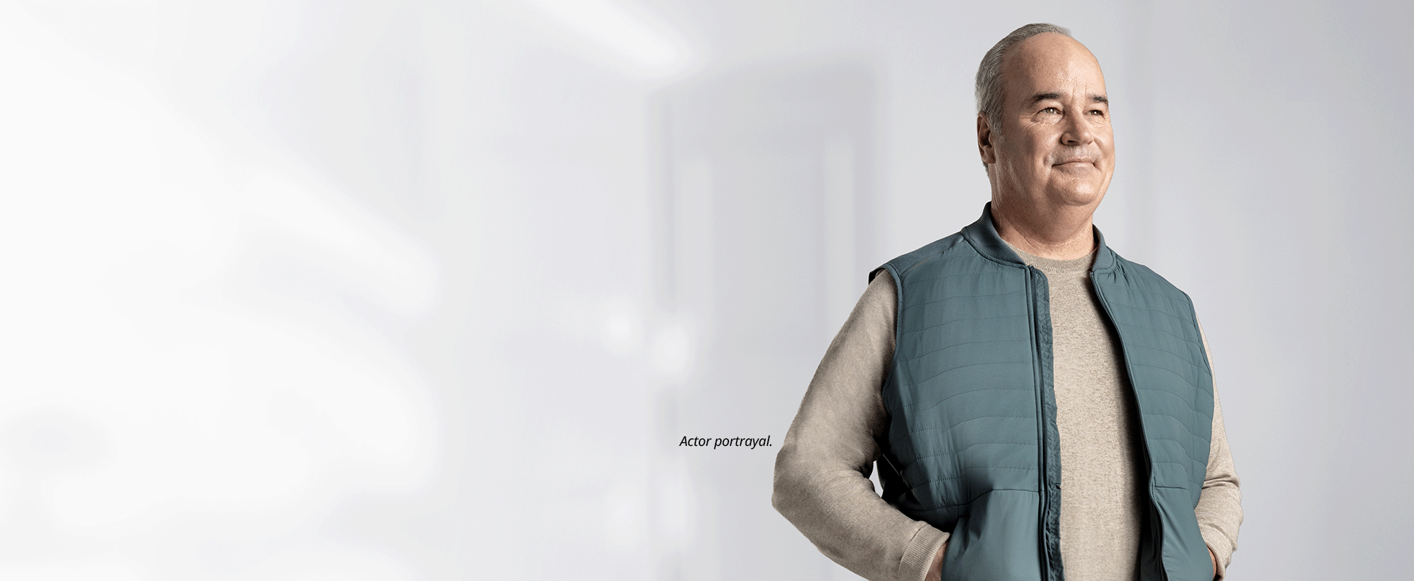 An older man smiling into the distance with his hands in his pockets. The footnote next to him reads: Actor portrayal.