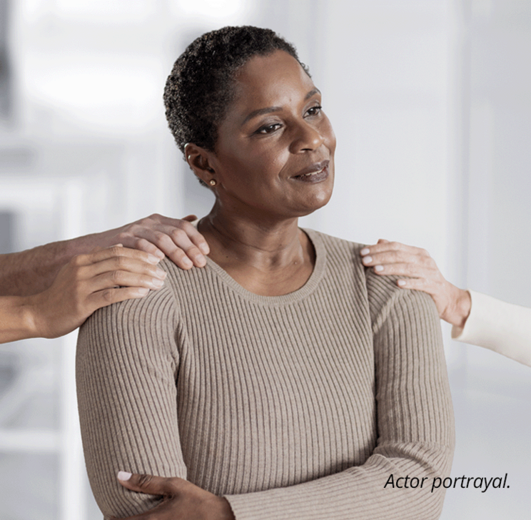 An older woman standing confidently with her arms crossed. Hands reach out from both sides of the frame and touch her shoulders, showing her support. The footnote next to her reads: Actor portrayal.